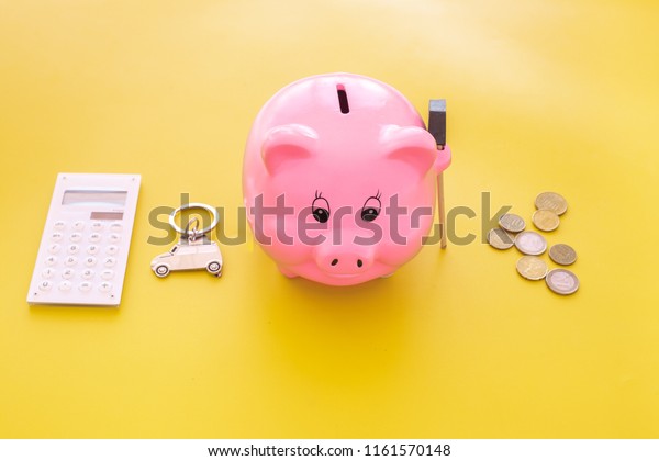 Money for buy car. Moneybox in shape of pig near\
keychain in shape of car, coins, calculator on yellow background\
copy space