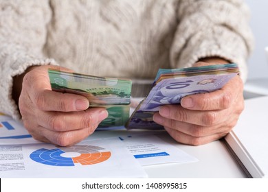 Money From Canada. Dollars. Canadian Currency. Retired Woman Holding Bill On Desk Office.