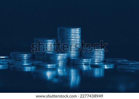 Money coin stack on office desk with blue filter. Business and finance concept.