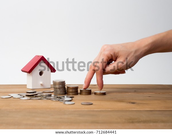 Money coins stack growing with red house on wood\
background. Business growth investment and financial concept\
ideas.Real estate investment. House and coins on table.Save money\
with stack coin.