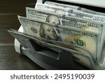 Money counter machine with dollar banknotes on wooden table, closeup