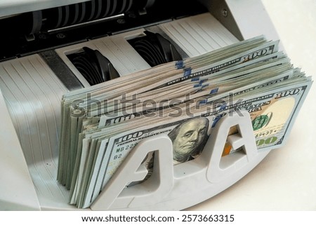 A money counting machine processes stacks of hundred-dollar bills in a busy financial office during working hours, demonstrating efficiency in cash handling.