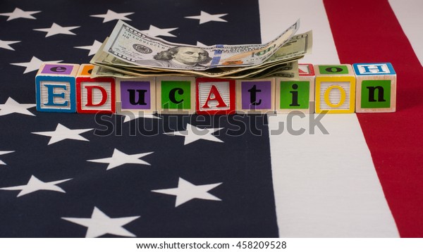 Money\
and education in America.  A pile of cash on top of letter blocks\
that spell education, on top of an American flag. \
