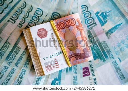 a lot of money with a face value of five thousand Russian rubles in the background of the entire photograph and a stack of money with a face value of one thousand Russian rubles tied with an elastic b