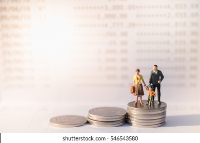 Money, Financial, Business Growth And Family  Concept, Miniature Figures Businessman, Woman And Child Stand On Top Of Stack Of Coins In Front Of Book Bank Under Morning Sun Light