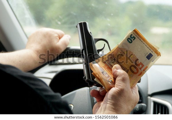     Money and a gun\
in the hands of a man who sits behind the wheel of a car.          \
                