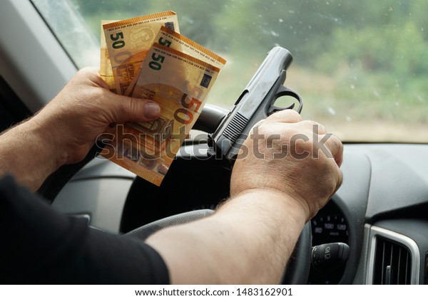 Money and a gun in the men\'s hands that lie on the\
steering wheel of a car.