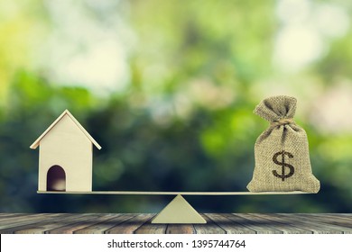 Money and home,loan,mortgage. Change home into cash concept. US Dollar in sack bag, Wooden house model put on scales on wood table with green tree bokeh as background. Balance home and debt.