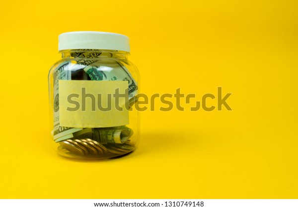Money jar with coins\
and paper dollars with sticker for your text, copy space. Isolated\
on yellow background