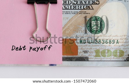 Money management saving plan - Dollars cash money clipped with pink note written DEBT PAYOFF - concept of money set aside to pay off debt