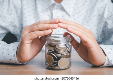 Money on glass jar under hands in gesture of protection on wooden desk, donation, saving, fundraising charity, family finance plan concept, superannuation, financial crisis concept