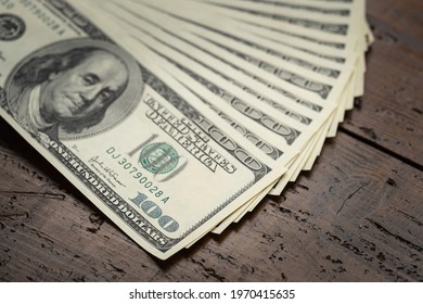 A money pile of fan stacked one hundred US banknotes with president Franklin portrait over wooden table background. Cash of hundred dollar bills, paper money currency.