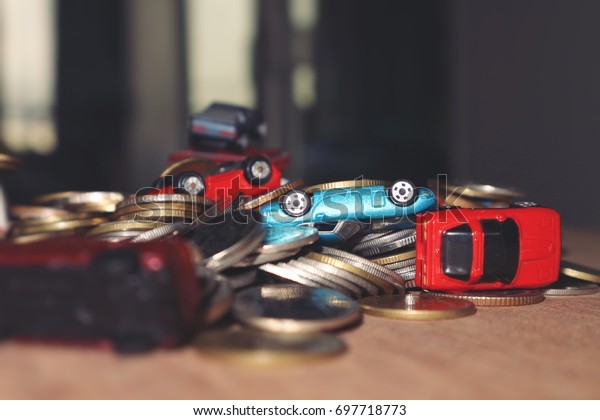 Money problem concept, toy cars overturn upside down on\
pile of coins money on wood table, blur and dark low light\
background 
