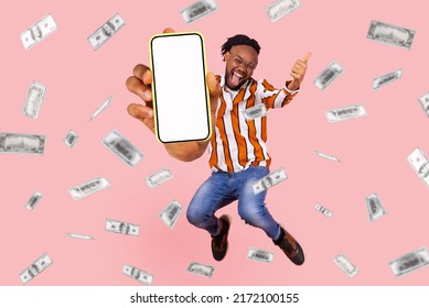 Money Rain And Rich Full Length Man Jumping Showing Phone Display. Extremely Excited Man Showing Thumbs Up Highly Jumping, With Mobile Phone Display. Indoor Studio Shot Isolated On Pink Background