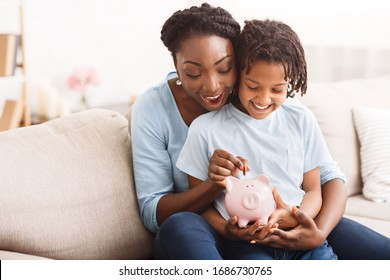 Money Saving Concept. Excited Black Mom And Daughter Putting Coins Into Piggy Bank, Free Space