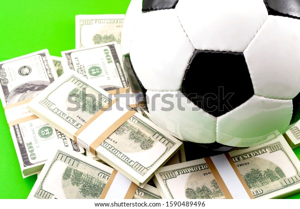 Money in sports, football\
match fixing and betting on the outcome of sporting event\
conceptual idea with soccer ball on pile of dollars isolated on\
green background