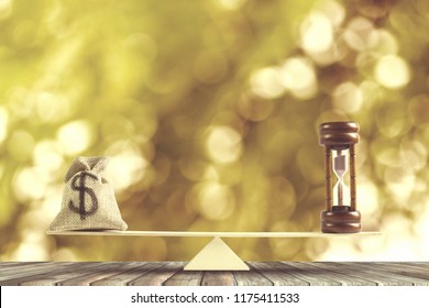 Money And Time Balance, Change Money Into Cash Or Reverse Concept : US Dollar In Sack Bag, Hourglass Put On Scales On Wood Table With Golden Bokeh As Background. Golden Time Or Money.