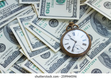 money and time concept - old pocket watch on pile of american dollars