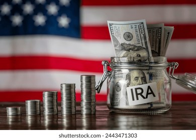 Money towers and glass jar used for saving US dollar bills and notes for IRA retirement fund on the American flag background, close up. Finance, business, investment and money saving concept