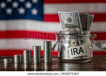 Money towers and glass jar used for saving US dollar bills and notes for IRA retirement fund on the American flag background, close up. Finance, business, investment and money saving concept