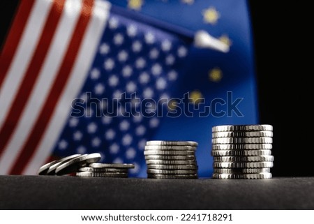 Money of the United States and Europe and two Flags on a dark background. It is a symbol of the United States of America increasing tariff tax barriers for import products from EU countries.
