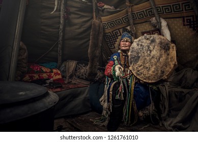 Mongolia shaman doing authentic ritual of summoning spirits. shaman with jewelry holding drum with incense. Shamanic ritual in winter. Ethnic traditions