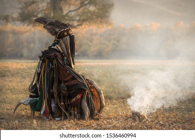 Mongolian traditional shaman performing a traditional shamanistic ritual with a drum and smoke in a forest during autumn afternoon. Ulaanbaatar, Mongolia.