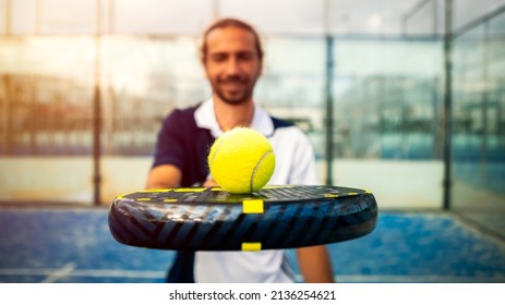 Monitor Of Padel Holding Black Racket With Yellow Tennis Ball Over. Class To Student On Outdoor Tennis Court. Man Paddel Player Playing A Match In The Open