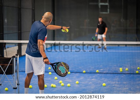 Monitor teaching padel class to man, his student - Trainer teaches boy how to play padel on indoor tennis court