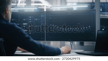 Monitoring Big Data Metrics in Server Hall. Professional Male Manager Sitting at Desk Monitors Performance Metrics on Dual Screens Against Backdrop of Server Racks. Management and Big Data Analysis.