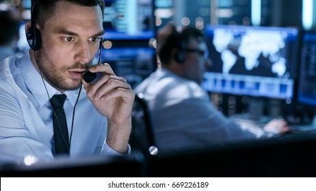 In Monitoring Room Technical Support Specialist Speaks into Headset. His Colleagues are Working in the Background. - Shutterstock ID 669226189