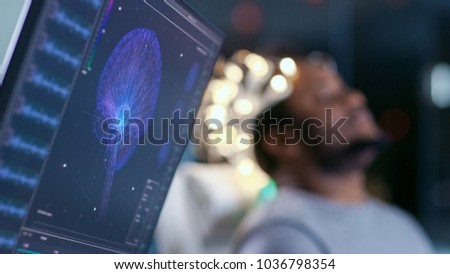 Monitors Show EEG Reading and Graphical Brain Model. In the Background Laboratory Man Wearing Brainwave Scanning Headset Sits in a Chair with Closed Eyes. In the Modern Brain Study Research Laboratory