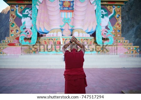 A monk holding hands & praying in front of a giant Maitreya Buddha statue, in North India.