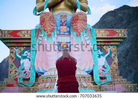 A monk praying in front of a giant Buddha statue, in North India.