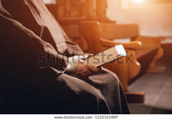 A monk in robes with holy bible in their hands\
praying in the church.\
Background