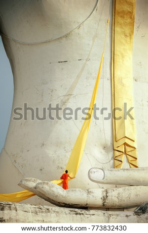 A monk standing on the palm of a big Buddha statue, he is preparing yellow robe to wrap around the statue.