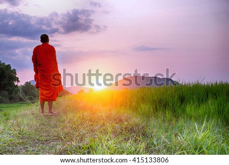 A Monk walks a path towards a setting sun in Cambodia or could be any South East Asian country. This monk's face is not shown and could be any monk.
