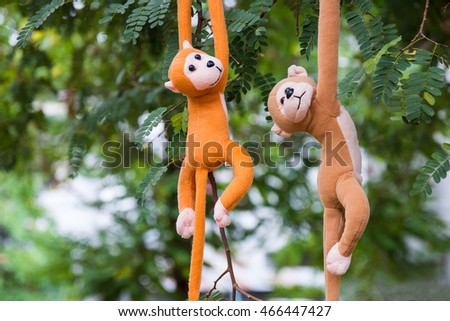 Monkey small teddy perched on a green tree background. Toys cute made of fabric scraps. Brown sock stuffed for child.