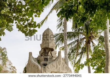 A monkey stands on a decorated temple structure with carved details surrounded by tropical trees in Thailand.
