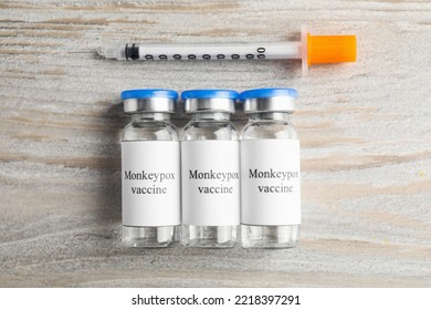 Monkeypox Vaccine In Glass Vials And Syringe On Wooden Table, Flat Lay