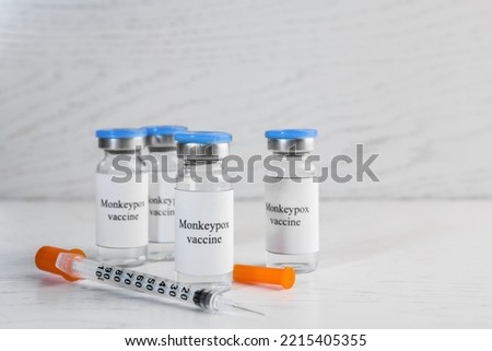 Monkeypox vaccine in glass vials and syringe on white wooden table, space for text