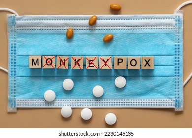 The monkeypox virus is laid out with wooden cubes on a surgical face mask. There are various pills lying around. Renaming the disease monkeypox to MPOX. The letters are crossed out with a red cross. - Shutterstock ID 2230146135