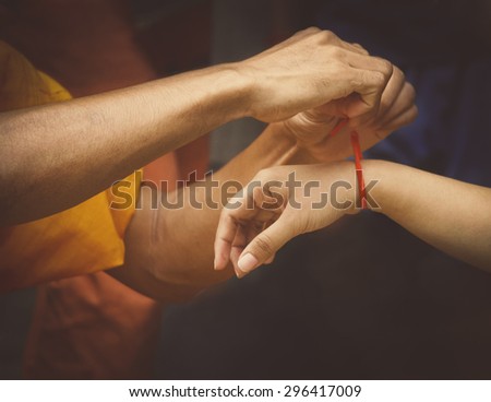 monks giving blessings for peace & luck by tie white or red cotton type string around the wrist of people in Cambodia, Laos, Thailand