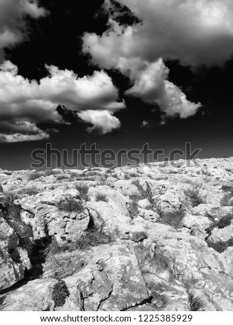 monochome surreal image of a harsh rocky nanscape in bright light with dark contrasting sky and white clouds
