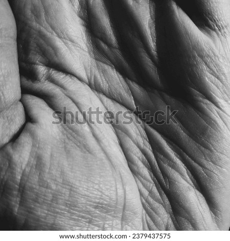 A monochromatic close-up of a clenched hand, showcasing skin texture, imprints, and wrinkles.