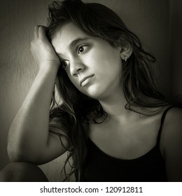 Monochromatic Portrait Of A Sad Hispanic Girl Sitting In A Corner With A Dirty Wall Background