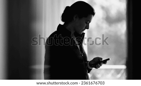 Monochromatic scene of woman using smartphone device browsing internet on cellphone, person staring at screen