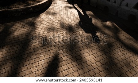 Monochromatic, silhouette legs and long shadows across an ancient cobbled street in early evening setting sunlight