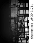 A monochrome abstract view of a fire escape structure, showcasing intricate metal bars and shadows against a light background. The composition emphasizes lines and geometric shapes.