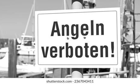Monochrome close-up of a sign in the sunshine in a harbor with the words "Fishing prohibited!" written in German script - Shutterstock ID 2367043411